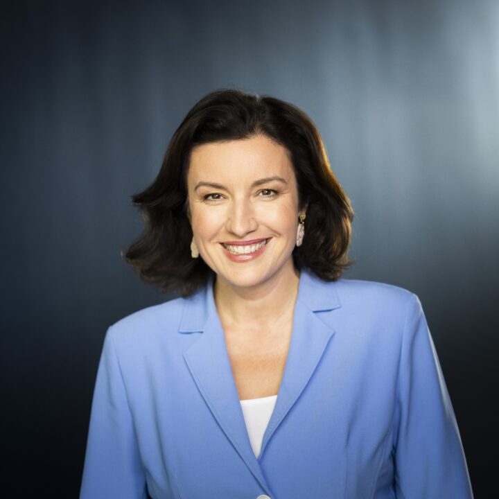 Dorothee Bär im blauen Blazer vor einer grauen Wand. Sie lächelt.