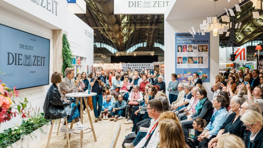 Viele Menschen sitzen im Halbkreis und hören zwei Personen bei einem Interview zu vor dem ZEIT-Stand.
