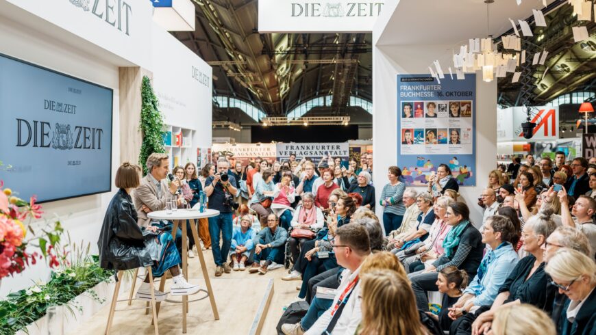 Viele Menschen sitzen im Halbkreis und hören zwei Personen bei einem Interview zu vor dem ZEIT-Stand.